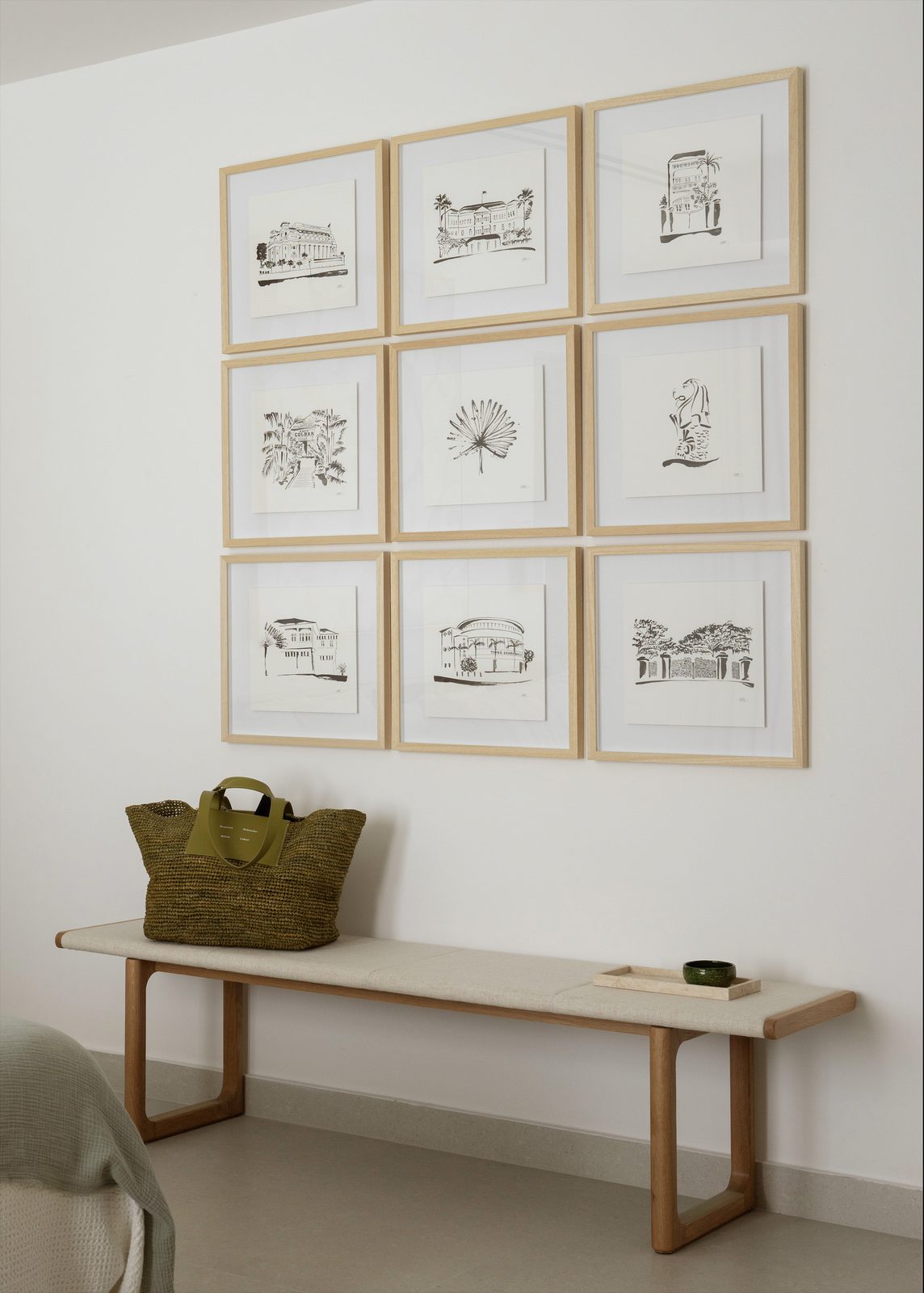 Framed line-drawing prints on a white wall above a console and a green woven bag